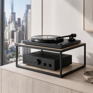 Op de afbeelding: Een zwarte platenspeler met een vinylplaat staat op de bovenste plank van een tweelaagse standaard van zwart metaal en licht hout. Een zwarte audioversterker met meerdere ronde bedieningsknoppen staat op de onderste plank van de standaard.