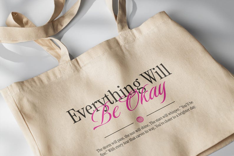 May include: A beige canvas tote bag with black and pink text that reads "Everything Will Be Okay". The text is accompanied by a quote: "The storm will pass, the sun will shine, The stars will whisper, "You'll be fine." With every tear that carves its way, You're closer to a brighter day."
