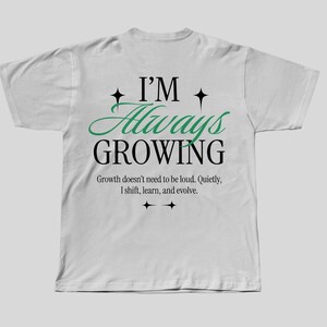 May include: White t-shirt with a green and black graphic that says "I'm Always Growing". The graphic also includes the text "Growth doesn't need to be loud. Quietly, I shift, learn, and evolve."