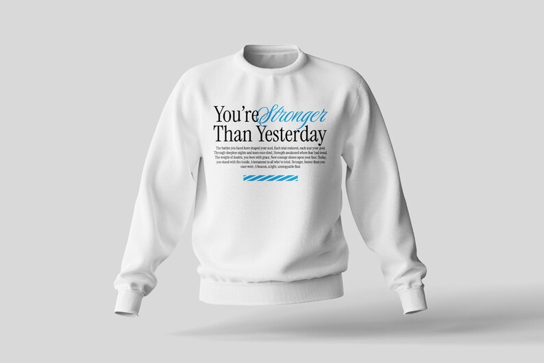 May include: White crewneck sweatshirt with the text "You're Stronger Than Yesterday" printed in black with blue accents. The text is surrounded by a small paragraph of text.