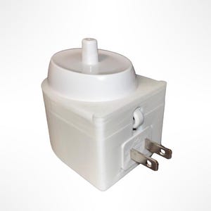 May include: A white, rectangular electrical plug-in device with a rounded top and a small, cylindrical protrusion. The device has two metal prongs for insertion into a standard electrical outlet.