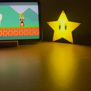 May include: A yellow star-shaped night light with a cartoon face and two black eyes. The light is on and illuminating the surrounding area.