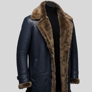 May include: A navy blue coat featuring a wide, brown faux fur collar and interior lining. The coat has long sleeves with adjustable buckled straps at the cuffs, two vertical side pockets, and a front button closure with dark circular buttons.