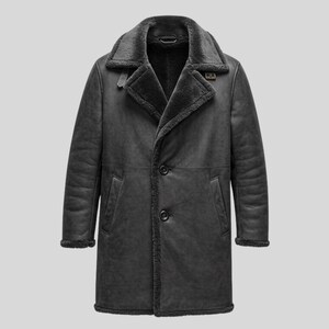 May include: A charcoal grey coat featuring a wide lapel collar lined with dark faux fur. The coat has long sleeves, two vertical side pockets, and a front closure secured by two dark buttons. The interior and edges are lined with dark faux fur.