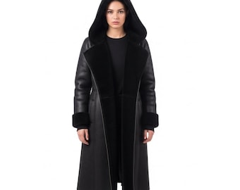 May include: A long, black hooded coat with a shearling lining and cuffs. The coat is made of leather and has a classic, tailored design. The model is wearing a black top underneath.
