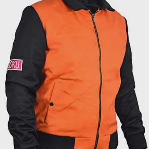 May include: Orange and black bomber jacket with a full-length zipper. The jacket has black sleeves and a black collar and waistband. A small patch with the text "GOKU" is on the left sleeve. The jacket is made of a smooth, possibly nylon, material.