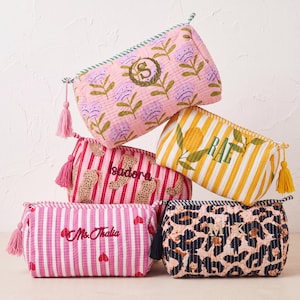 May include: A collection of five quilted fabric pouches featuring various patterns including pink flowers, yellow stripes with lemons, pink stripes with leopard spots, pink stripes with hearts, and a black and tan leopard print, each with a tassel zipper.