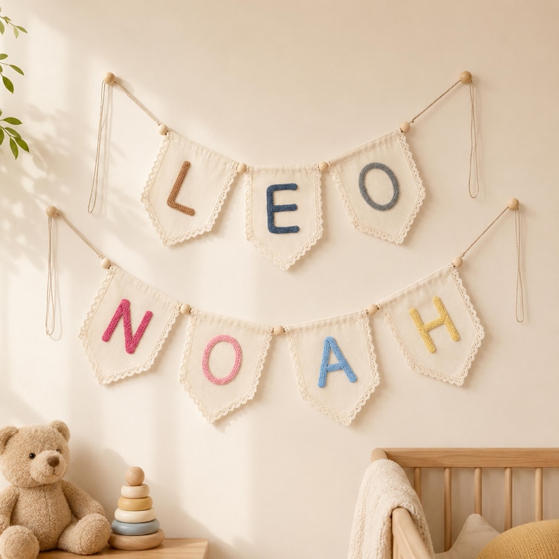 May include: Two rows of cream-colored fabric pennant banners hanging on strings with wooden beads. The top banner spells LEO with brown, dark blue, and grey letters. The bottom banner spells NOAH with pink, pink, blue, and yellow letters.