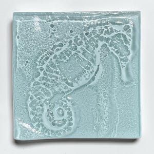 May include: Square, light blue glass tile with a seahorse design. The seahorse is raised and white, set against a textured background. The tile is a square shape, and the seahorse is in the center.