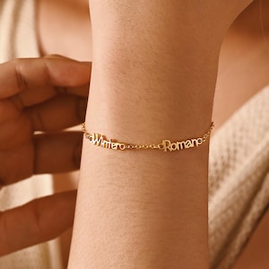 Puede incluir: Una delicada pulsera dorada con las palabras "Wintero" y "Romance" escritas en cursiva. La pulsera se lleva en la muñeca, con el texto claramente visible. La pulsera es una pieza de joyería.