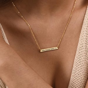 May include: A gold-colored necklace with a rectangular pendant. The pendant has the engraved text "Ride Around Gettin' It". The necklace is worn around the neck.