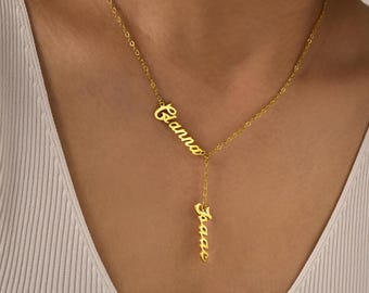 May include: A gold-colored, personalized necklace with two names, "Gianna" and "Isaac", in a delicate script font. The necklace has a Y-shaped design, with one name on the top and the other hanging below. The necklace is worn around the neck.