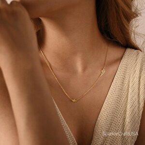 Puede incluir: Un delicado collar dorado con un peque&ntilde;o colgante de ala y una sola gema amarilla. El collar se lleva en el cuello de una persona, con la cadena apoyada en su piel. Una joya sencilla pero elegante.