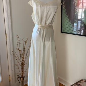 Pode incluir: Um vestido de camisola de cetim branco com decote em V e uma faixa na cintura.