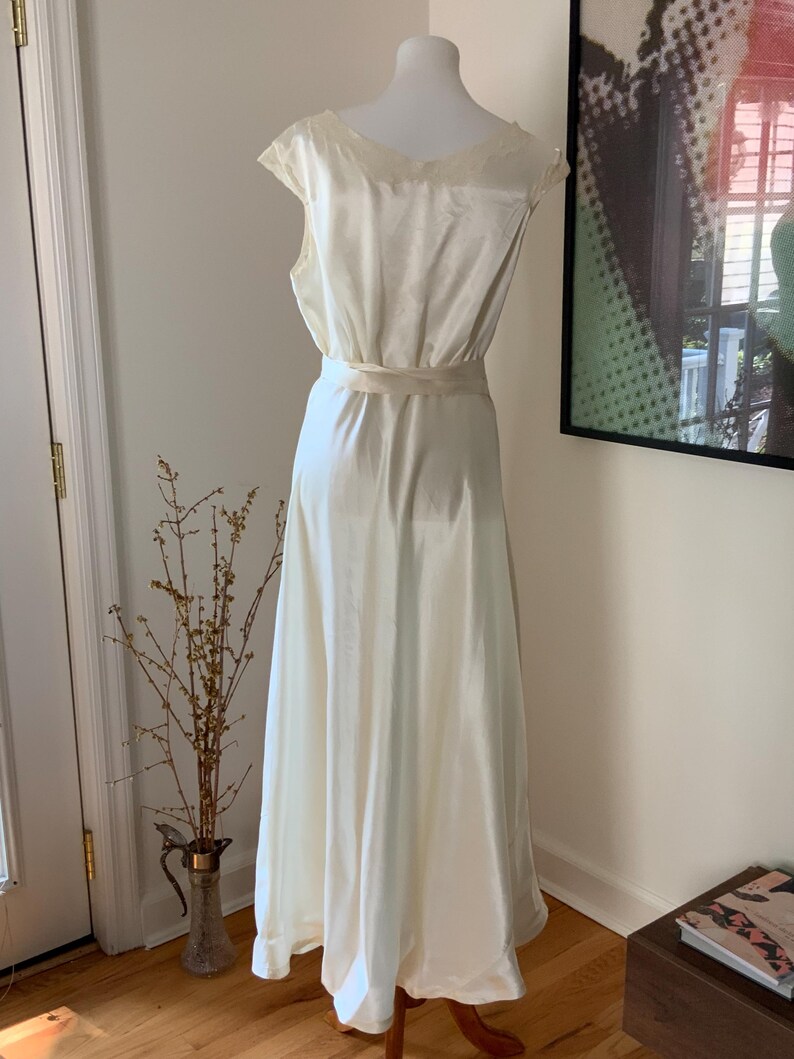 Pode incluir: Um vestido de camisola de cetim branco com decote em V e uma faixa na cintura.