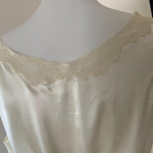 Pode incluir: Um camis&atilde;o de cetim branco com uma borda de renda ao redor do decote.