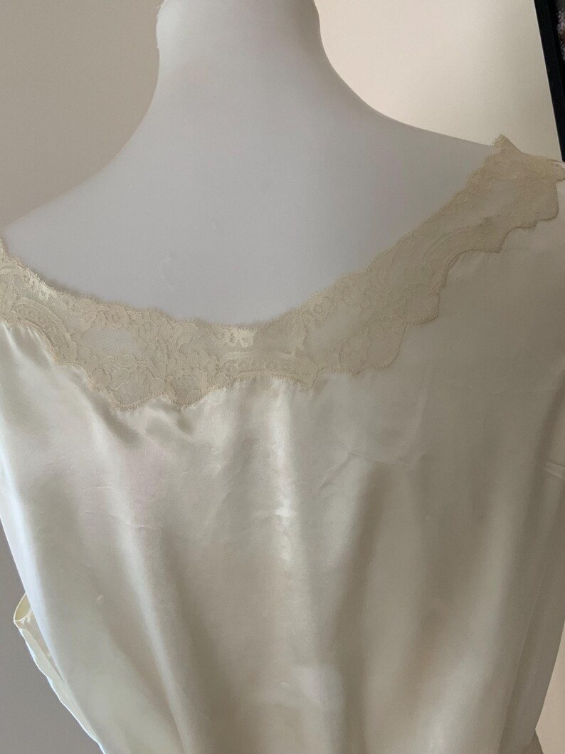 Pode incluir: Um camis&atilde;o de cetim branco com uma borda de renda ao redor do decote.