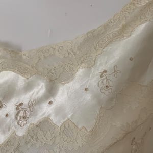 Pode incluir: Uma camisola de cetim branco com renda delicada e detalhes florais bordados.