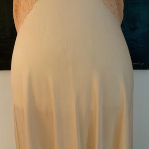 May include: A peach-colored slip dress with a delicate lace trim at the neckline. The dress is made of a soft, flowing fabric, and the lace adds a touch of elegance. The slip dress is a classic piece of lingerie.