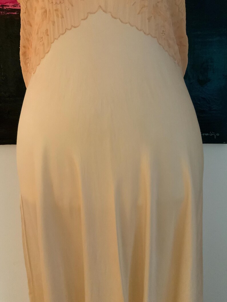 May include: A peach-colored slip dress with a delicate lace trim at the neckline. The dress is made of a soft, flowing fabric, and the lace adds a touch of elegance. The slip dress is a classic piece of lingerie.