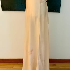 May include: A floor-length, cream-colored dress with a lace neckline. The dress has a flowing design and a subtle floral pattern near the hem. The dress is made of a soft, lightweight fabric.
