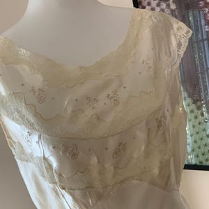 Pode incluir: Um vestido de camisola de cetim branco com renda delicada e detalhes florais bordados.