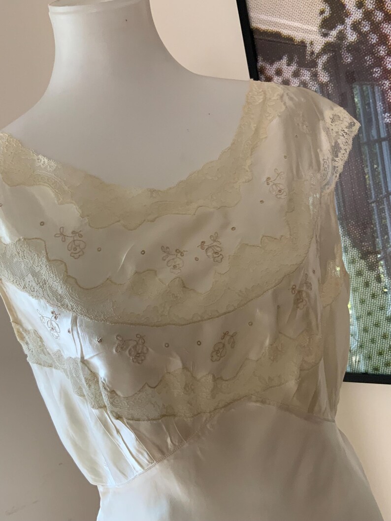 Pode incluir: Um vestido de camisola de cetim branco com renda delicada e detalhes florais bordados.
