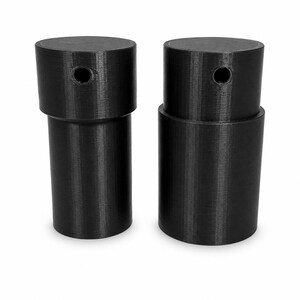 Peut inclure: Deux objets cylindriques noirs avec une conception étagée. Chaque pièce présente une section supérieure plus large avec un petit trou circulaire sur le côté et une base plus étroite. La surface a une texture en couches visible.