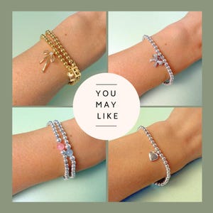 May include: Four bracelets are displayed, each worn on a wrist. One is gold with a bow charm, another silver with a bow charm, a third silver with pink and blue beads, and the last silver with a heart charm. The text "YOU MAY LIKE" is in the center.