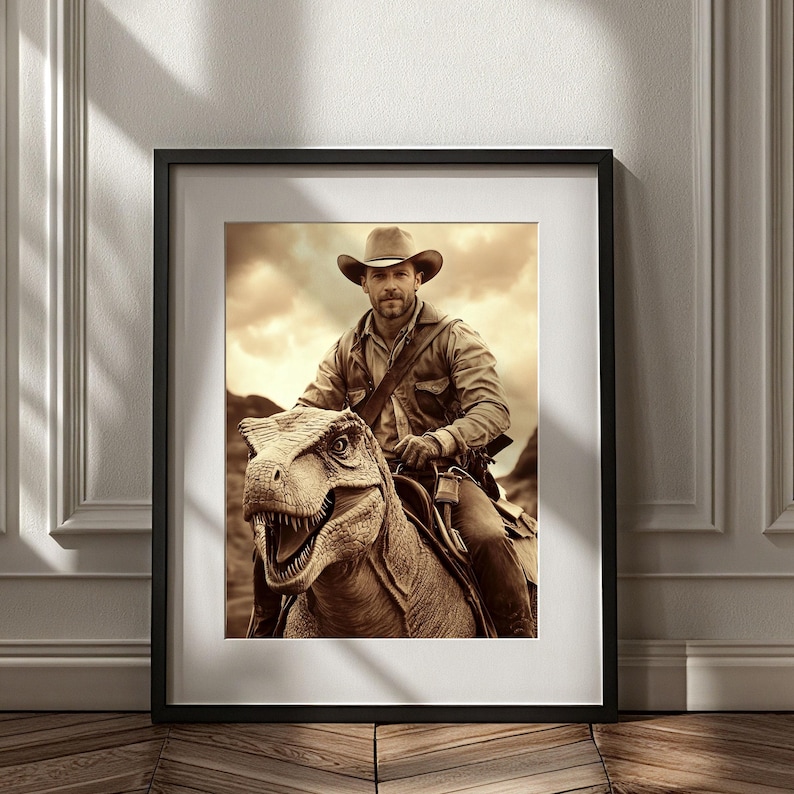 Op de afbeelding: Ingelijste sepia-kleurige print met een cowboy die op een dinosaurus rijdt. De cowboy draagt een hoed en een overhemd. De dinosaurus heeft zijn mond open, met tanden zichtbaar. De achtergrond toont een bewolkte lucht en bergen. De print zit in een zwarte lijst.