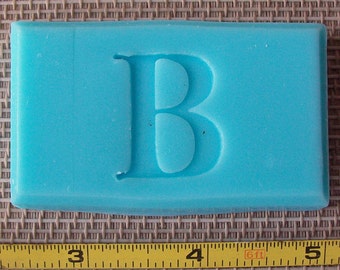 Può includere: Un blocco rettangolare di colore azzurro con la lettera "B" in rilievo in bianco.