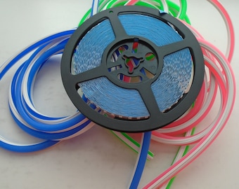 May include: A spool of blue LED light strip with a white and pink LED light strip wrapped around it. The spool is black and has a white label with the text "LED Strip Light".