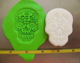 May include: Green silicone mold with a white sugar skull design. The mold is approximately 3 inches wide.