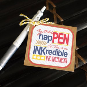 Puede incluir: Una tarjeta marrón con rayas blancas y el texto "you hapPEN to be an INKredible TEACHER" con tres manzanas amarillas. La tarjeta está atada a un bolígrafo plateado con una cuerda amarilla y blanca.