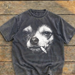 May include: Dark gray t-shirt featuring a white graphic of a dog with a cigarette in its mouth. The shirt has a vintage wash and the words "Worn Heritage Vintage Wear" are printed on the bottom right.