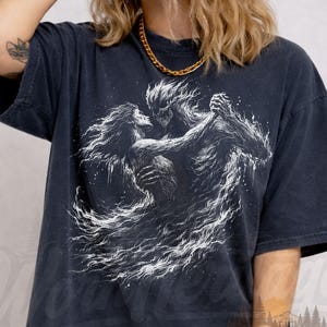 May include: Black comfort colors t-shirt featuring a white graphic of two figures embracing, with flowing, ethereal details. The shirt has a vintage wear design and the text "Worn Heritage" is visible.