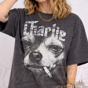 Könnte beinhalten: Dunkelgraues T-Shirt mit einem schwarz-weißen Grafikdruck eines Hundes mit Zigarette und dem Schriftzug "Charlie". Das Shirt hat einen Vintage-Look.