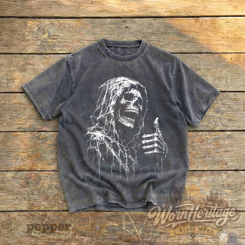 Op de afbeelding: Een antracietgrijs t-shirt met korte mouwen en een witte grafische print van een skelet met capuchon en een spinnenwebtextuur. Het skelet is afgebeeld met een open mond en een skeletachtige hand die een duim omhoog gebaar maakt op de voorkant.