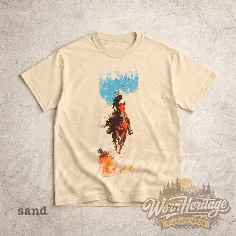 May include: Sand-coloured t-shirt with a graphic of a cowboy riding a horse, set against a blue sky and flames. The shirt includes the text "Worn Heritage Vintage Wear" at the bottom, in a vintage style.