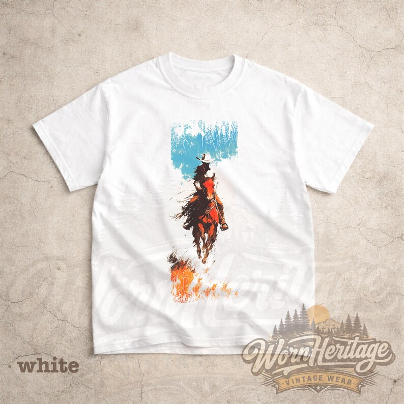 May include: White t-shirt with a graphic of a cowboy on horseback, set against a blue and white backdrop. The design includes a cowboy hat and flames at the bottom. The text "Worn Heritage Vintage Wear" is at the bottom.
