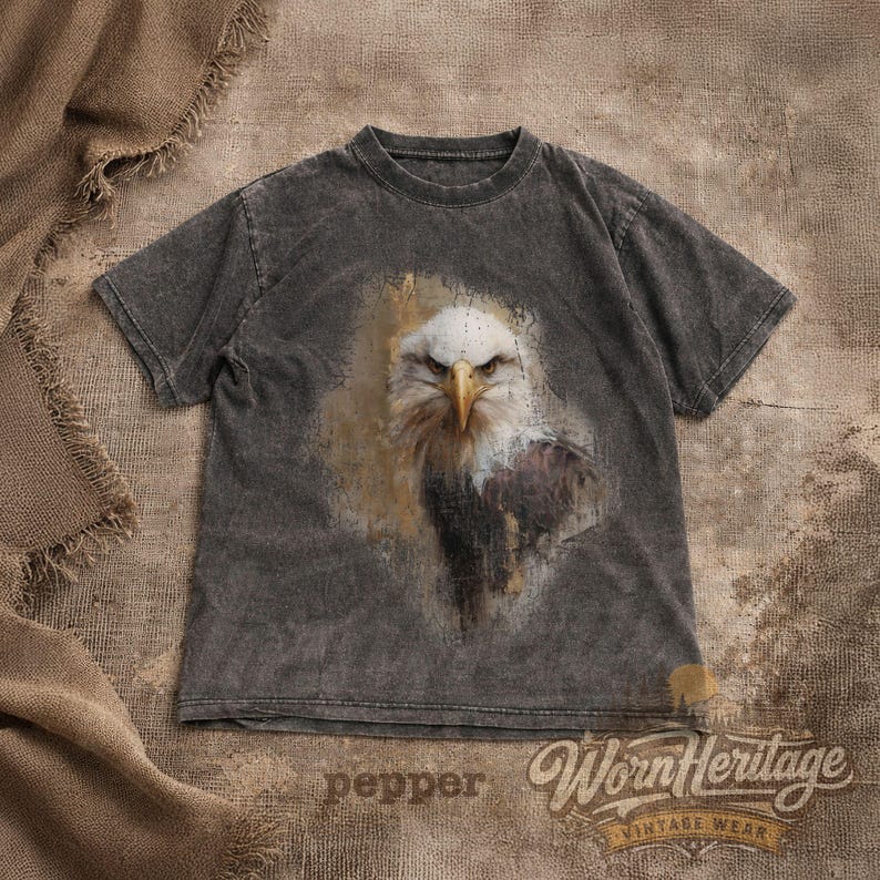 May include: Dark gray t-shirt featuring a detailed illustration of an eagle's head. The eagle has white feathers, a yellow beak, and a focused gaze. The shirt has the text "pepper" and "Worn Heritage Vintage Wear" printed on it.