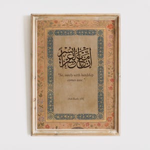 May include: Framed artwork featuring ornate calligraphy in black ink on a tan background. The frame is a light beige with floral and blue decorative borders. The text reads "So, surely with hardship comes ease." and "[Ash-Shath-05]"