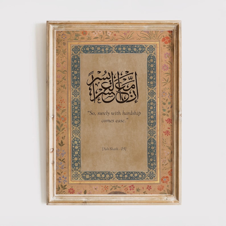May include: Framed artwork featuring ornate calligraphy in black ink on a tan background. The frame is a light beige with floral and blue decorative borders. The text reads "So, surely with hardship comes ease." and "[Ash-Shath-05]"