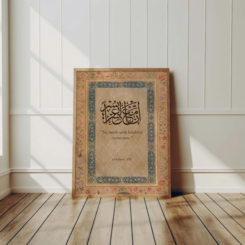May include: A framed print with ornate borders and Arabic calligraphy. The print features a central text in elegant script, with the English translation "So, surely with hardship comes ease." The frame has a floral design.