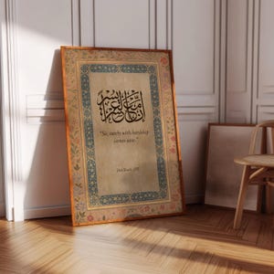 May include: Framed artwork with ornate borders and Arabic calligraphy. The text reads, "So, surely with hardship comes ease." The frame is a warm brown, and the artwork has a vintage, aged appearance. The background is a neutral color.