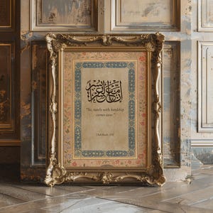 May include: A framed print with ornate gold detailing. The print features Arabic calligraphy in black ink, with the English translation "So, surely with hardship comes ease." The frame has a floral and geometric border.
