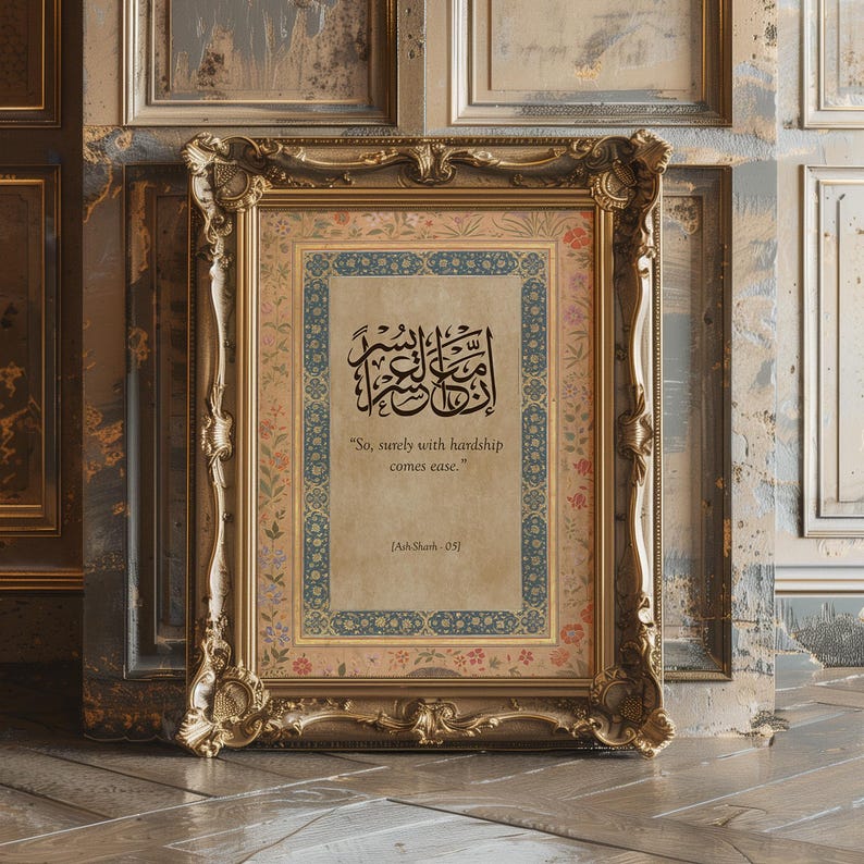 May include: A framed print with ornate gold detailing. The print features Arabic calligraphy in black ink, with the English translation "So, surely with hardship comes ease." The frame has a floral and geometric border.