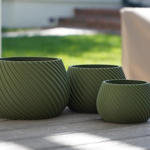 May include: Three green ceramic planters with a swirl design. The planters are arranged in a row from largest to smallest.