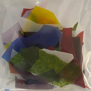 May include: A bag of assorted glass pieces in various colors, including green, blue, red, yellow, and purple. The pieces are irregular in shape and size.