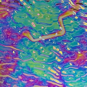 May include: A square sheet of iridescent glass featuring a rippled, water-like texture. The surface displays a vibrant spectrum of colors, including deep blues, bright teals, vivid purples, and streaks of yellow, creating a reflective, shifting effect.